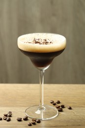 Delicious espresso martini in glass and coffee beans on wooden table