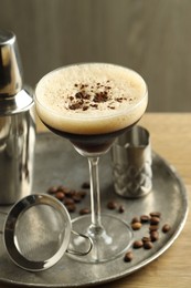 Photo of Tray with delicious espresso martini in glass, sieve, shaker and coffee beans on wooden table, closeup