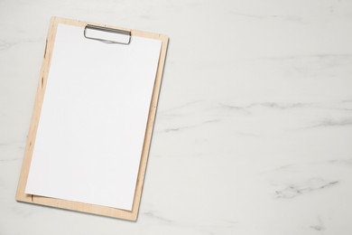 Photo of Clipboard with empty paper on white marble table, top view. Mockup for design