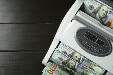 Photo of Money counter machine with dollar banknotes on wooden table, above view. Space for text