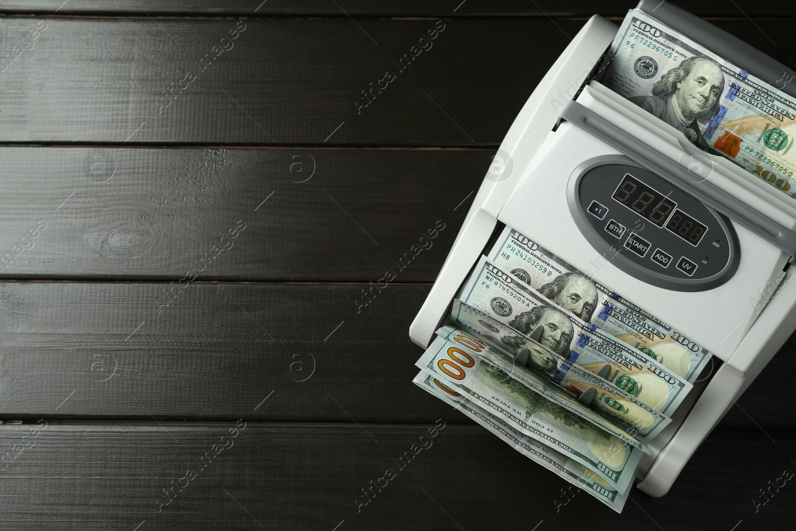 Photo of Money counter machine with dollar banknotes on wooden table, above view. Space for text