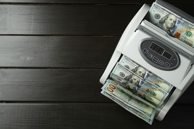 Photo of Money counter machine with dollar banknotes on wooden table, above view. Space for text