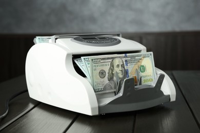 Photo of Money counter machine with dollar banknotes on wooden table