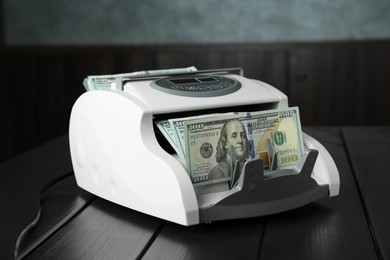 Photo of Money counter machine with dollar banknotes on wooden table