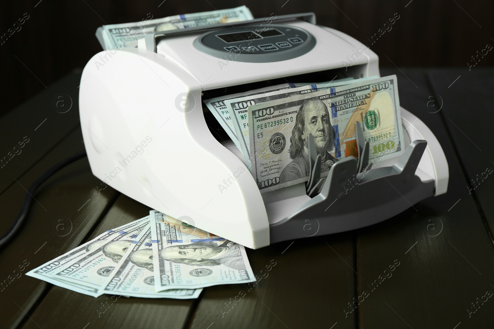 Photo of Money counter machine with dollar banknotes on wooden table