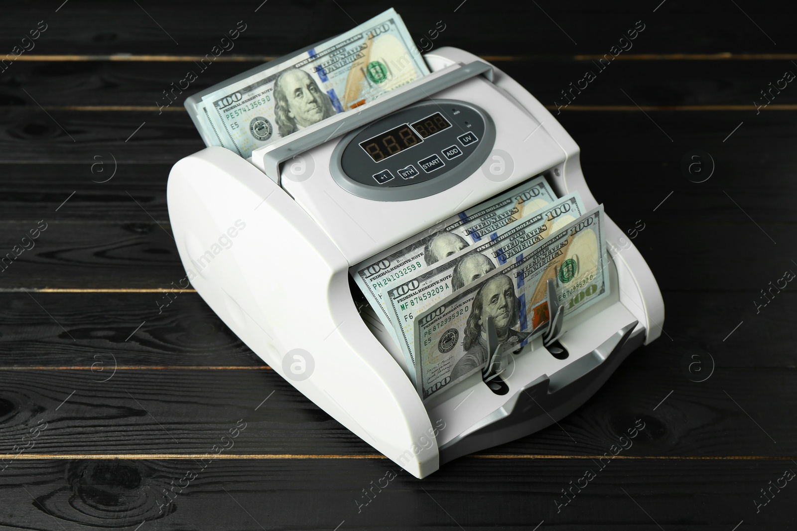 Photo of Money counter machine with dollar banknotes on black wooden table