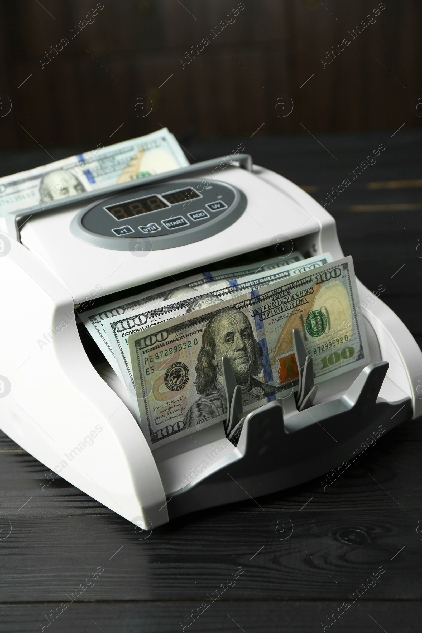 Photo of Money counter machine with dollar banknotes on black wooden table