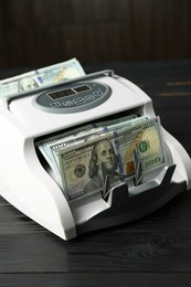 Photo of Money counter machine with dollar banknotes on black wooden table