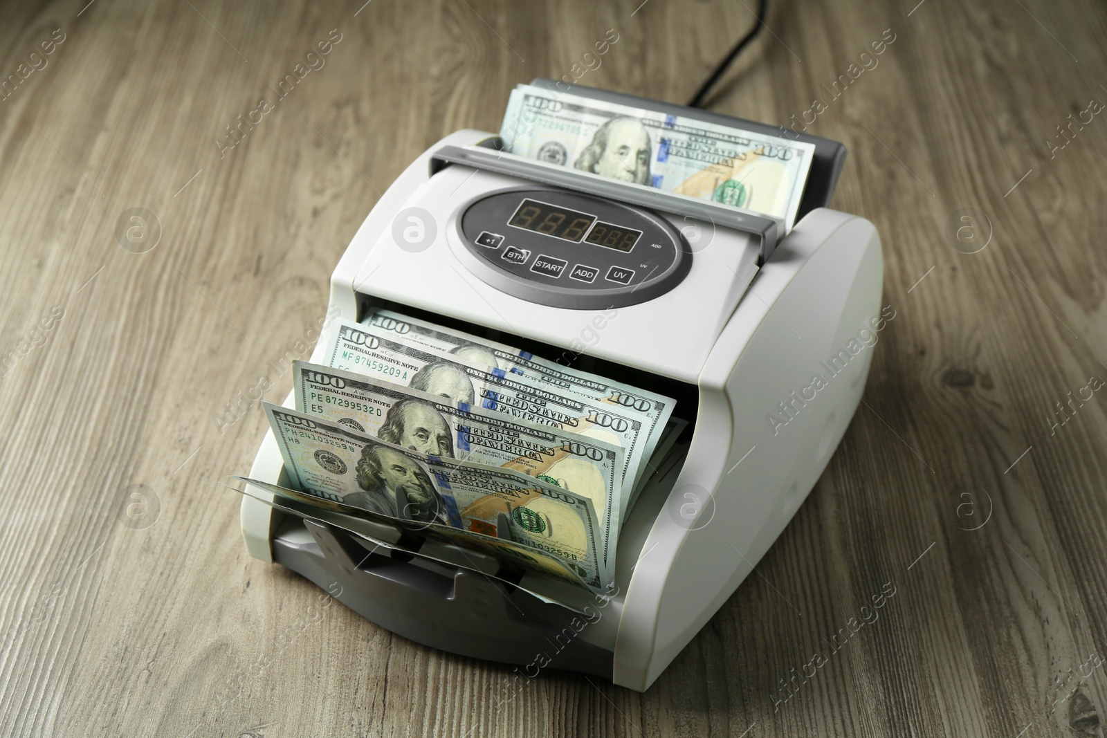 Photo of Money counter machine with dollar banknotes on wooden table