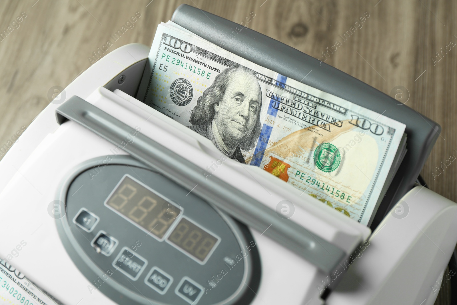 Photo of Money counter machine with dollar banknotes on wooden table, closeup