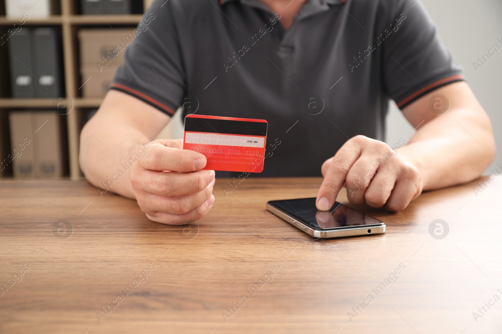 Photo of Man with credit card using smartphone at wooden table indoors, closeup