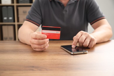 Photo of Man with credit card using smartphone at wooden table indoors, closeup