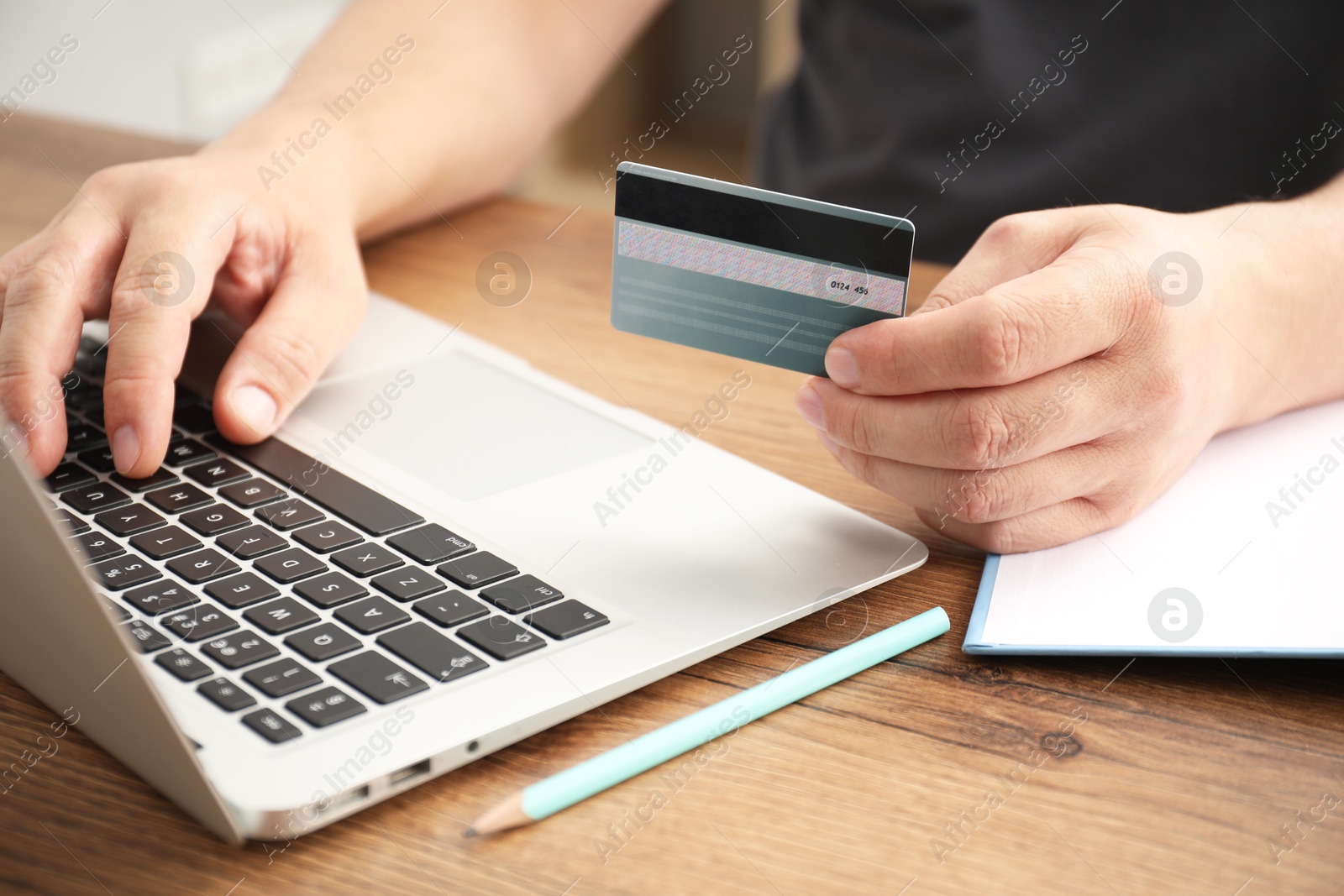 Photo of Man with credit card using laptop at wooden table indoors, closeup