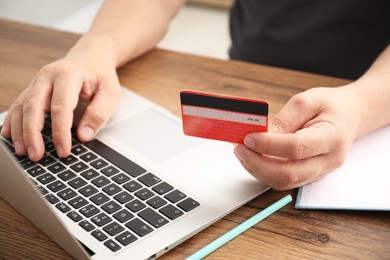 Photo of Man with credit card using laptop at wooden table indoors, closeup