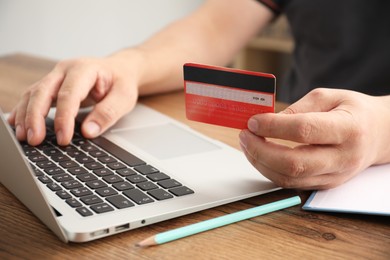 Photo of Man with credit card using laptop at wooden table indoors, closeup