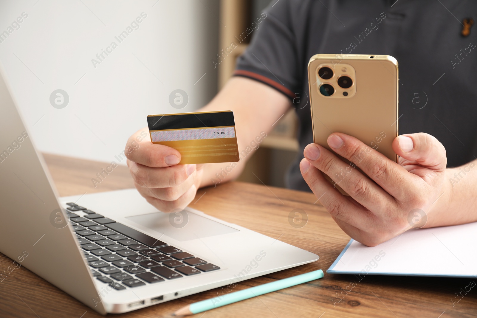 Photo of Man with credit card and smartphone at wooden table indoors, closeup