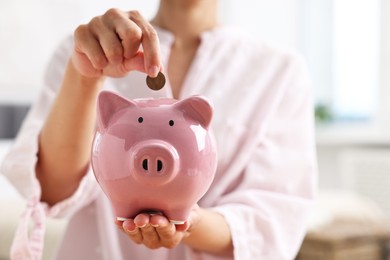 Photo of Woman putting coin into piggy bank indoors, closeup