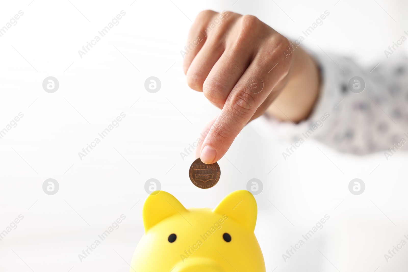 Photo of Woman putting coin into piggy bank indoors, closeup