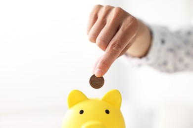 Photo of Woman putting coin into piggy bank indoors, closeup