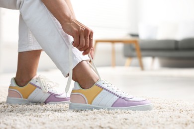 Photo of Woman tying shoelace of sneaker indoors, closeup