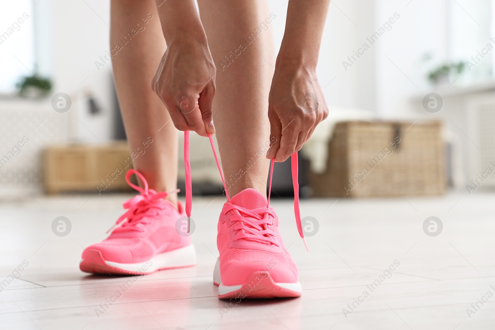 Photo of Woman tying shoelace of pink sneaker indoors, closeup. Space for text