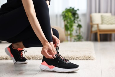 Photo of Woman tying shoelace of sneaker indoors, closeup. Space for text