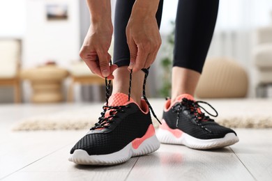 Woman tying shoelace of sneaker indoors, closeup