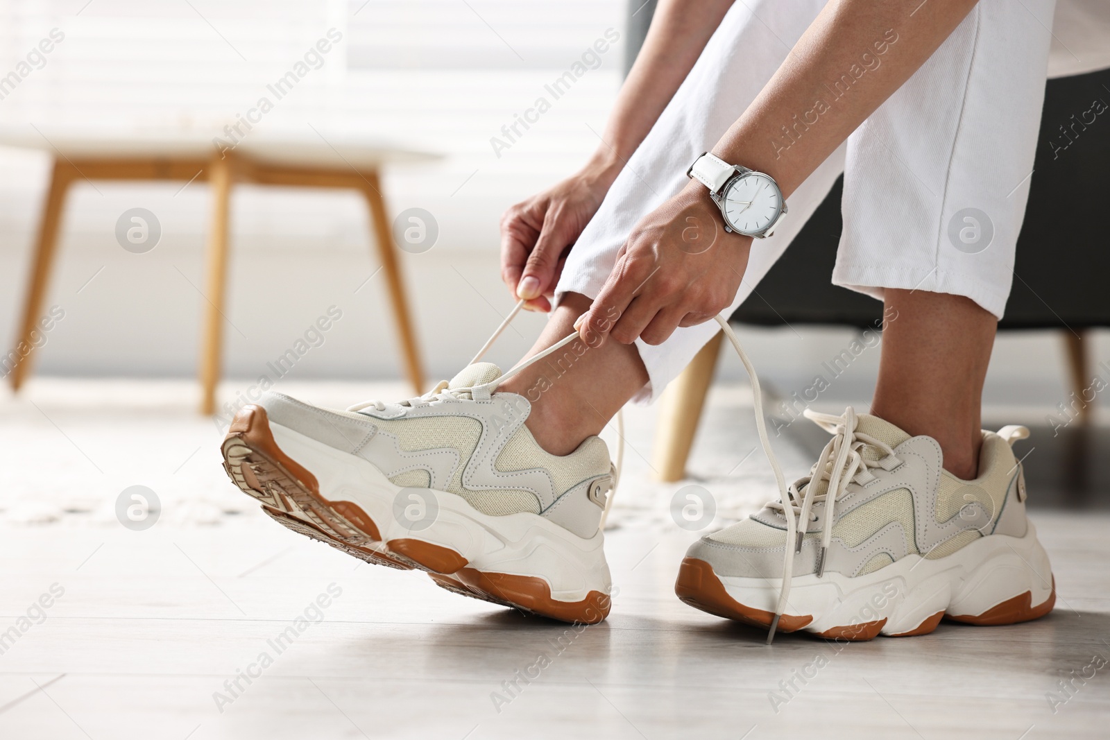 Photo of Woman tying shoelace of sneaker indoors, closeup