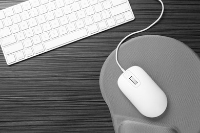 Photo of Computer mouse, mousepad and keyboard on black wooden table, flat lay