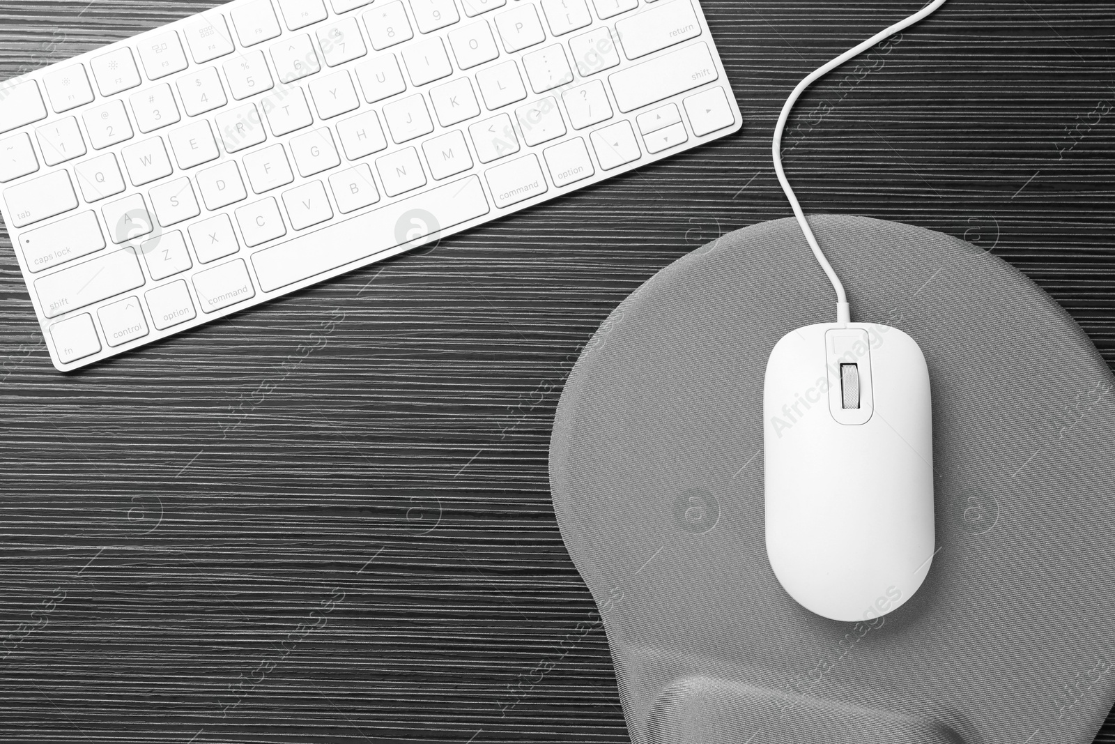 Photo of Computer mouse, mousepad and keyboard on black wooden table, flat lay