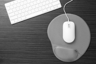 Photo of Computer mouse, mousepad with armrest and keyboard on black wooden table, flat lay