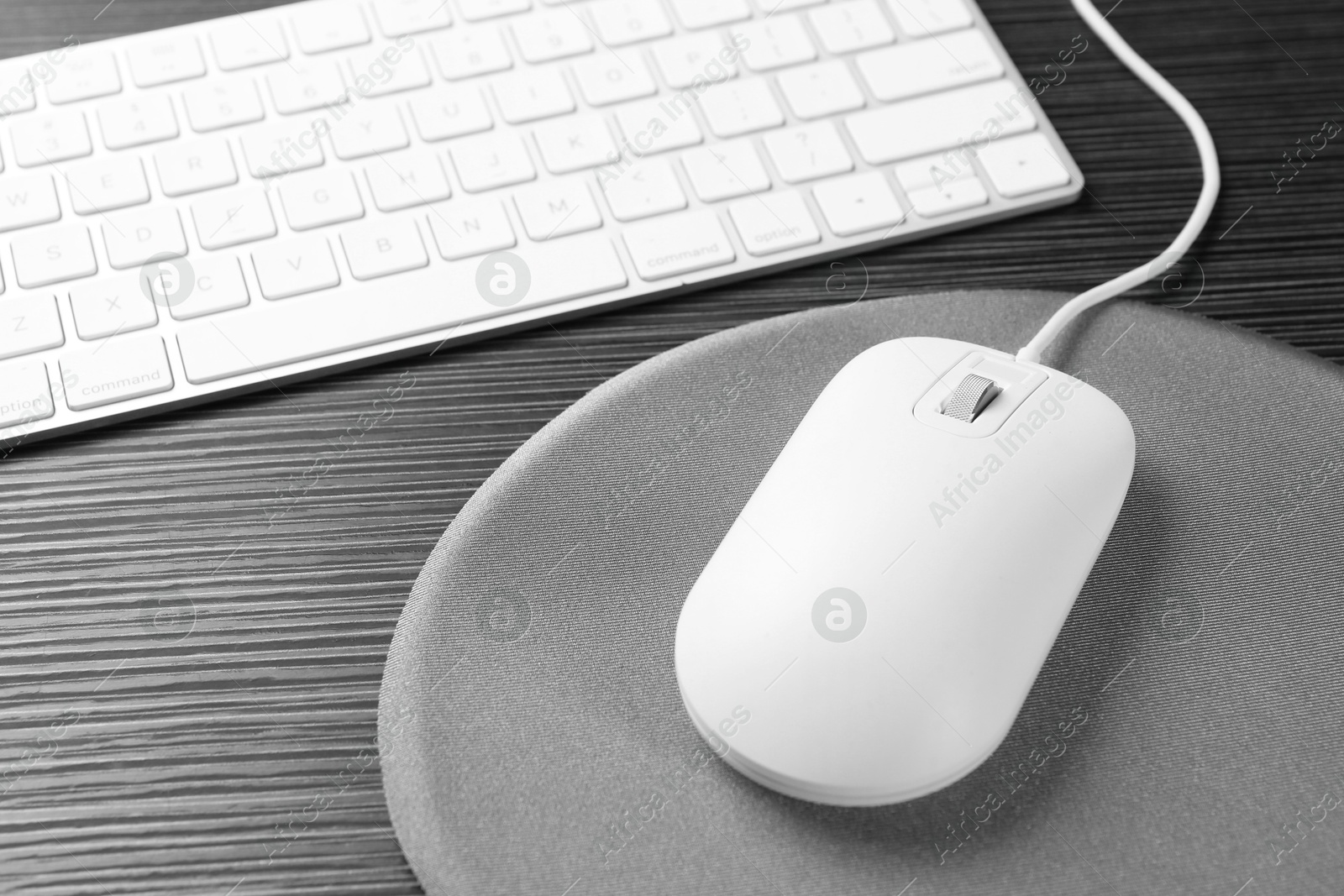 Photo of Computer mouse, mousepad and keyboard on black wooden table