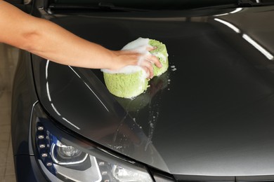 Man washing car hood with sponge indoors, closeup