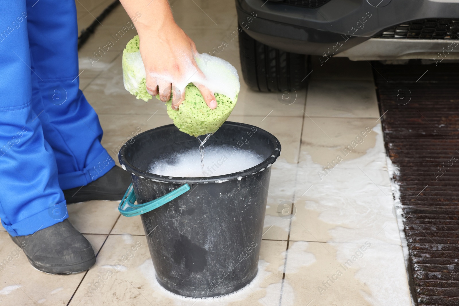 Photo of Man holding sponge with foam near basket at car wash, closeup