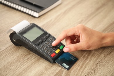 Photo of Woman using credit card terminal at wooden table, closeup