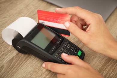 Photo of Woman with credit card using terminal at wooden table, closeup