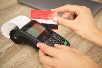 Photo of Woman with credit card using terminal at wooden table, closeup