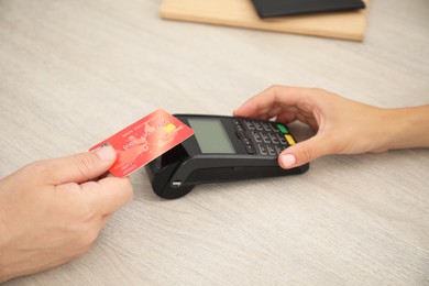 Photo of Woman taking payment from client via credit card terminal at wooden table, closeup