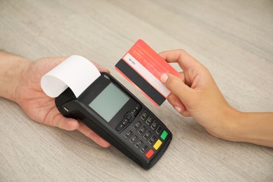 Photo of Man taking payment from client via credit card terminal at wooden table, closeup