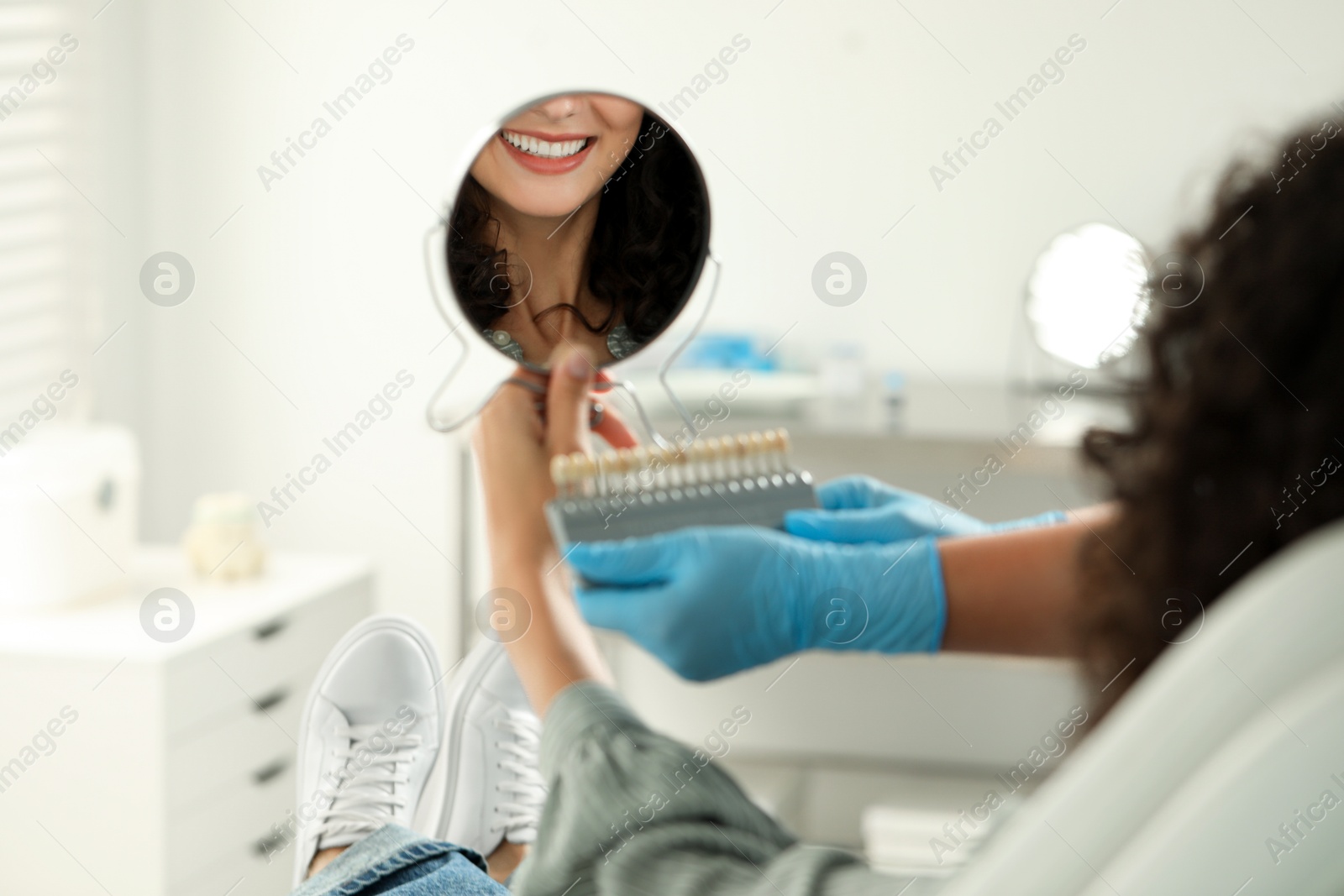 Photo of Patient looking in mirror while doctor holding teeth color chart in clinic, closeup. Dental veneers