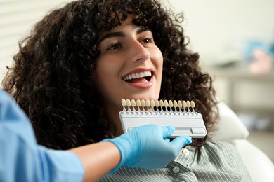 Photo of Doctor checking young woman's teeth color in clinic, closeup. Dental veneers