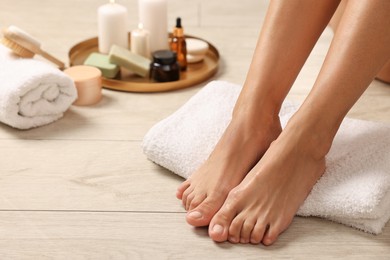 Photo of Woman with smooth feet, towel and other spa supplies on floor, closeup. Body care