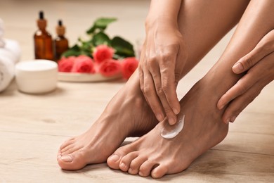 Woman applying moisturizing cream onto her feet on floor, closeup. Body care