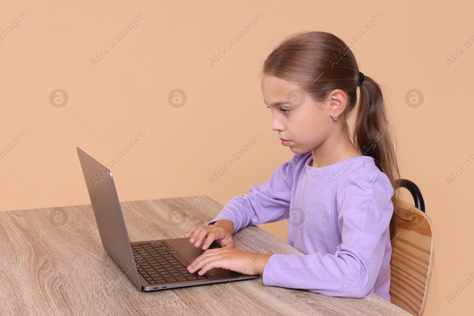 Photo of Girl with correct posture using laptop at wooden desk on beige background