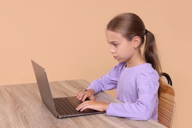 Girl with correct posture using laptop at wooden desk on beige background