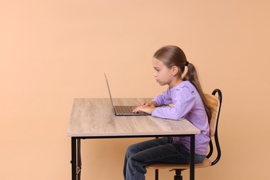 Girl with incorrect posture using laptop at wooden desk on beige background