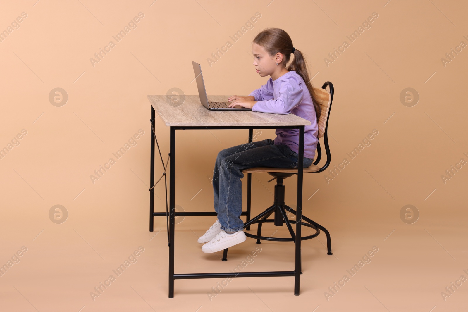 Photo of Girl with incorrect posture using laptop at wooden desk on beige background