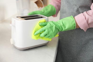 Photo of Woman wiping toaster with rag at countertop in kitchen, closeup