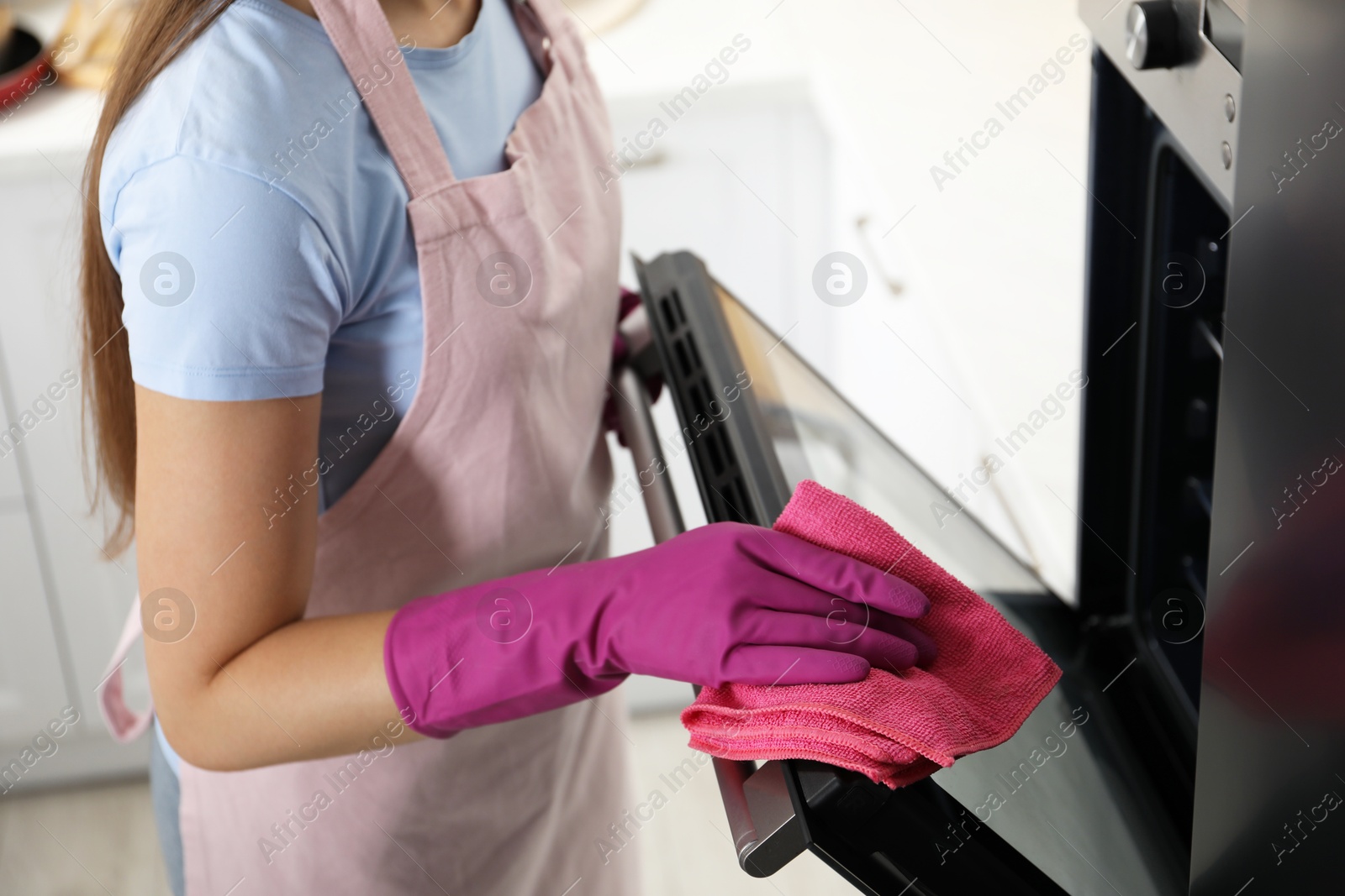 Photo of Woman wiping electric oven with rag in kitchen, closeup