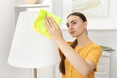 Beautiful young woman cleaning floor lamp with rag at home